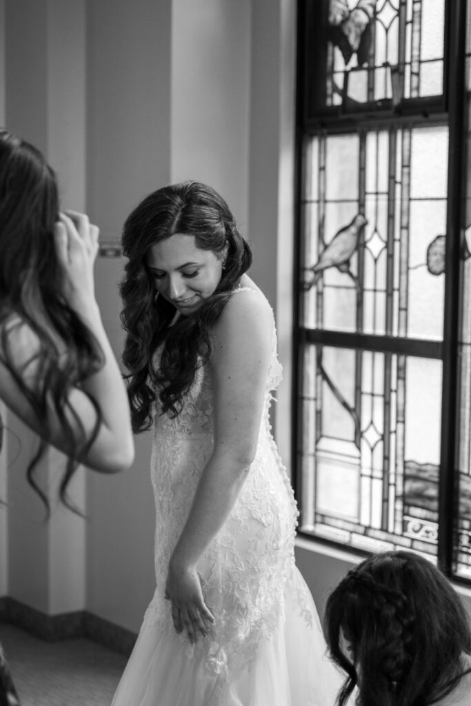 Catholic Bride looks down as her Maid of Honor adjusts the train of her dress before her California Catholic Wedding.