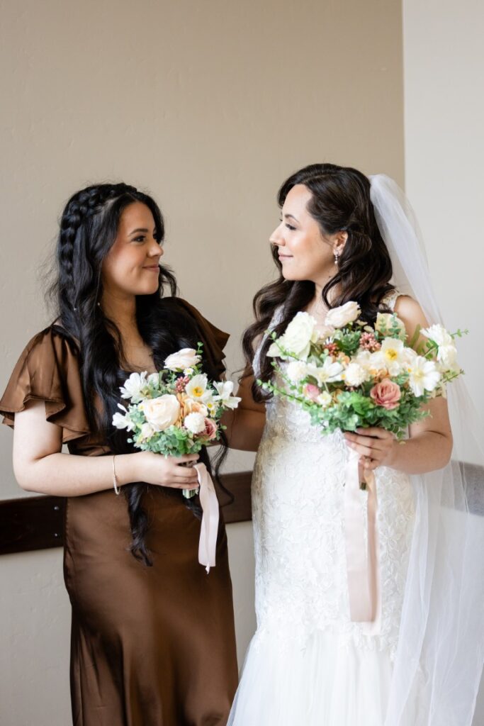 Catholic bride and Maid of Honor smile with bouquets of flowers before the California Catholic Wedding.