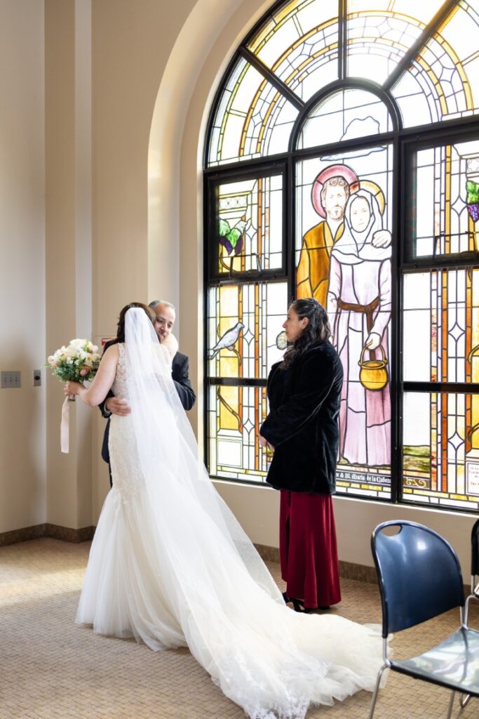 Catholic bride hugs father while mother watches before the California Catholic Wedding.