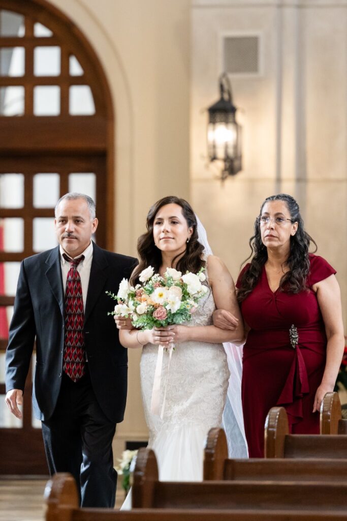 Catholic bride walks down the aisle with her parents.