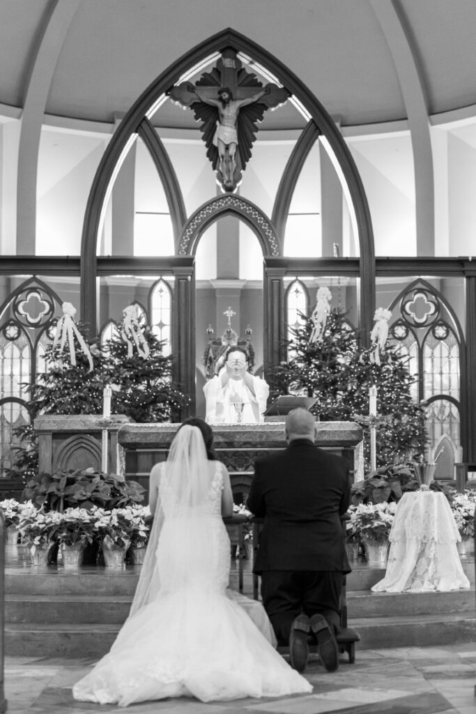 The priest elevates the Eucharist during the Eucharistic prayer with  bride and groom kneeling at the foot of the altar.