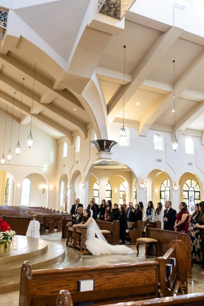 wide angle shot of the bride and groom kneeling at the altar.