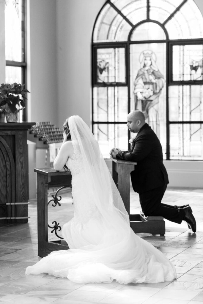 Catholic bride and groom praying at kneelers in front of a statue of Our Lady of Fatima.