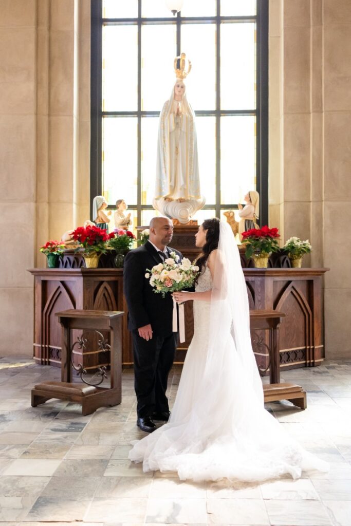 Catholic bride and groom in front of a statue of Our Lady of Fatima.